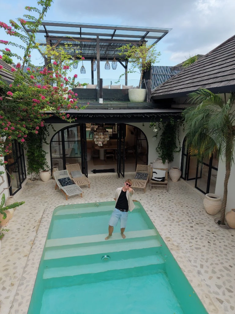Lukas in a villa pool courtyard pointing toward the camera